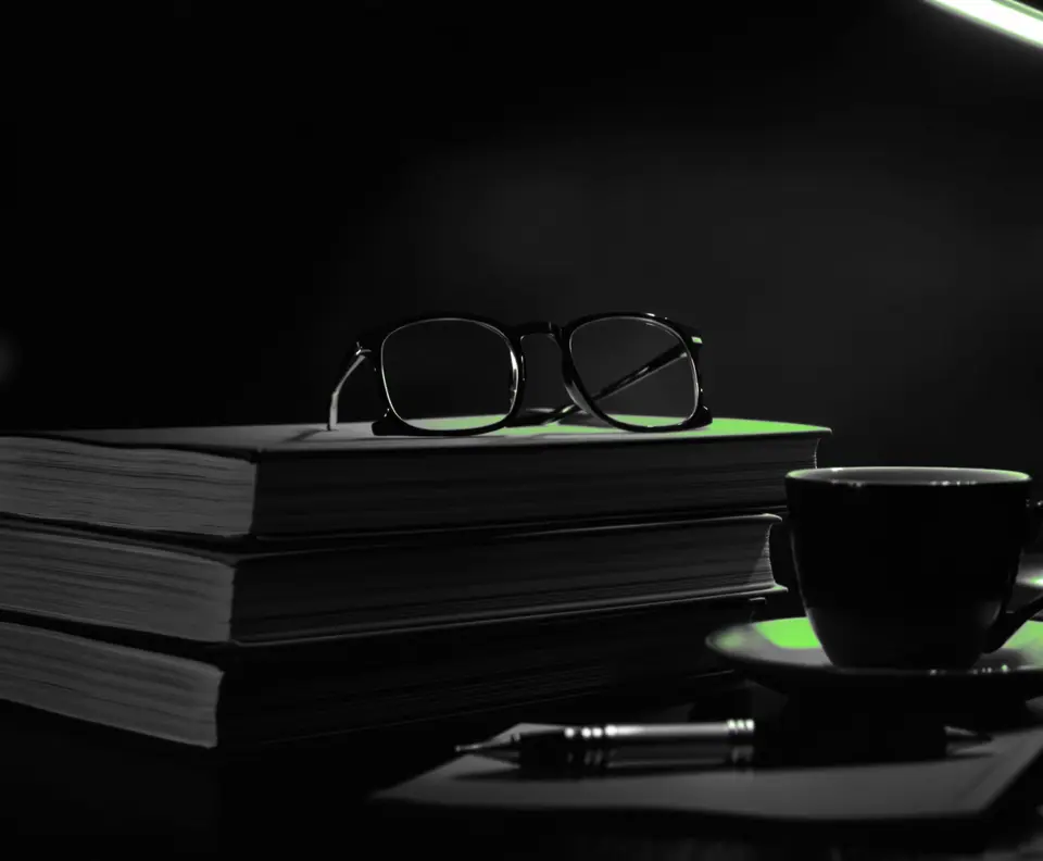 Libros apilados, gafas y una taza de café bajo una lámpara verde: portada del blog de marketing digital de DataLab
