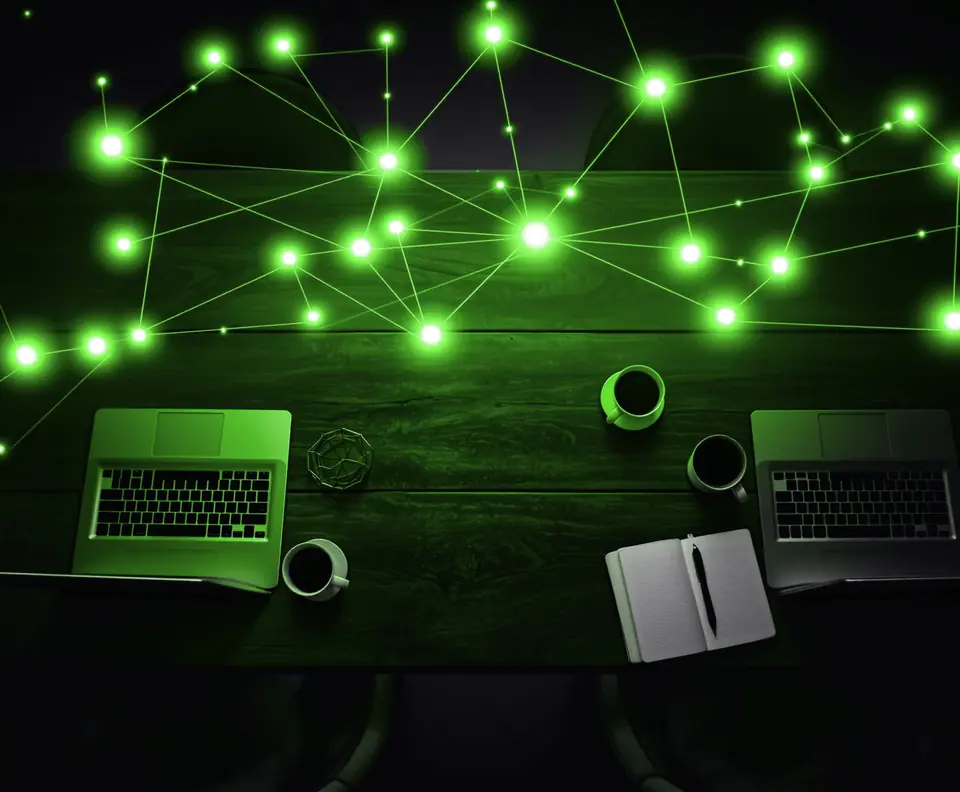 Vista cenital de una mesa con dos portátiles y cafés bajo una red de nodos de luz verde: caso de prospección en LinkedIn de DataLab
